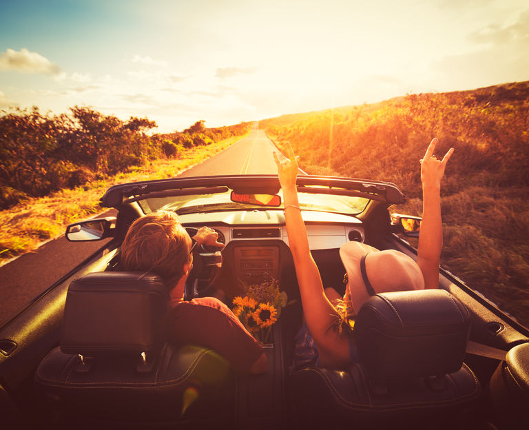 44098865 - young couple driving along country road in convertable at sunset